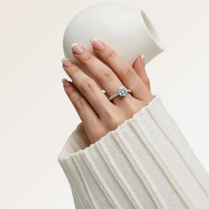 modell med tynn diamantring i hvitt gull med 2,00 carat diamant med små diamanter pavefattet i ringen holder en vase i hånden.