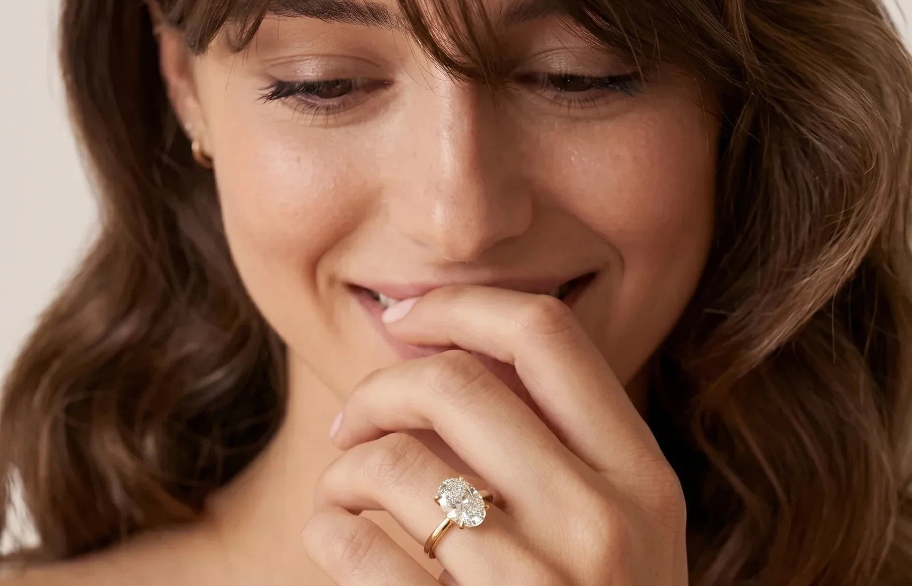 Smilende kvinne med hånden mot munnen og en oval forlovelsesring med lab-diamant i gult gull på fingeren
