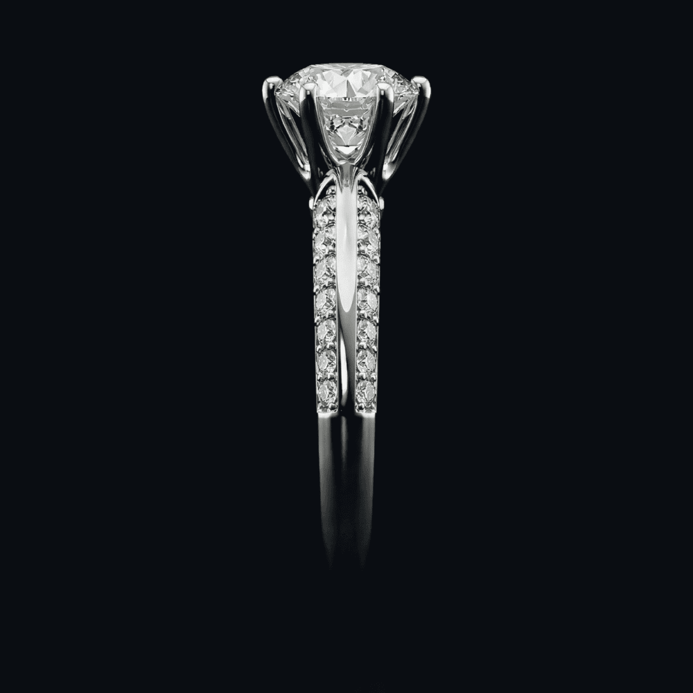 Ring med rund diamant i klør og pavé på skinnen, sett fra siden, mot sort bakgrunn