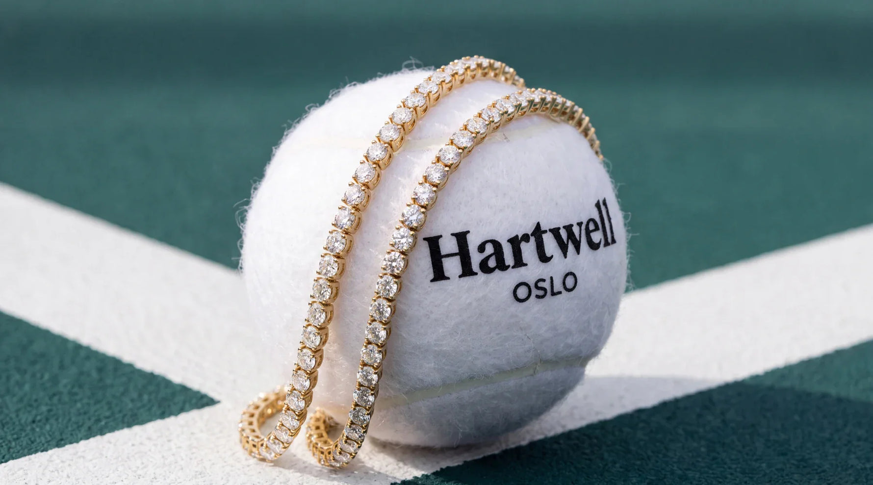 To tennisarmbånd i gult gull - på en hvit tennisballl med hartwell logo 