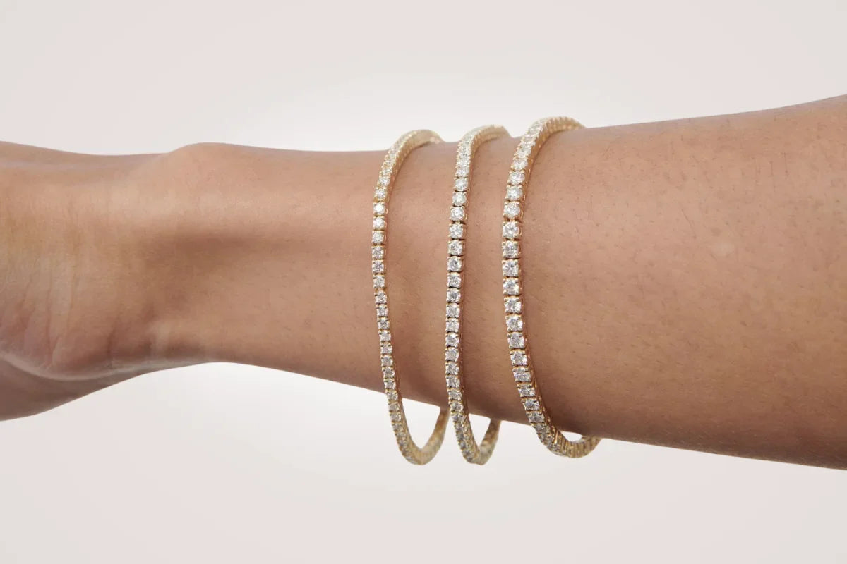 Arm med tre tennisarmbånd i gult gull fra Hartwell – lab diamant i ulike carat-størrelser for sammenligning.