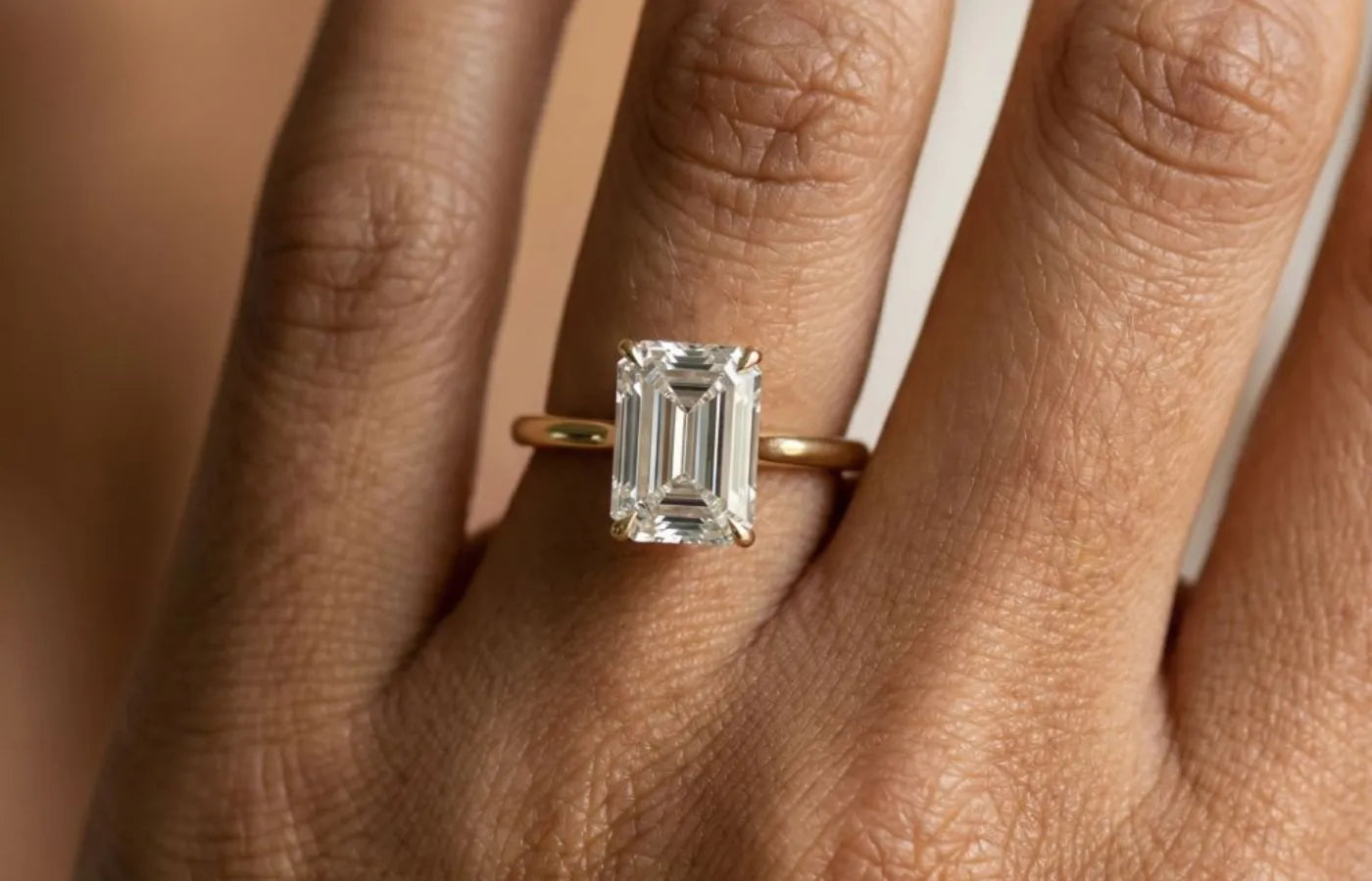 2 carat enerald cut diamantring i gult gull, nærbilde på fingeren til modell.