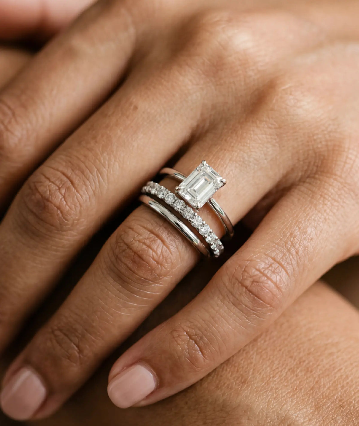 diamantring i hvitt gull med 1 carat emerald cut diamant - sammen med en evighetsring og giftering i hvitt gull, på finger.