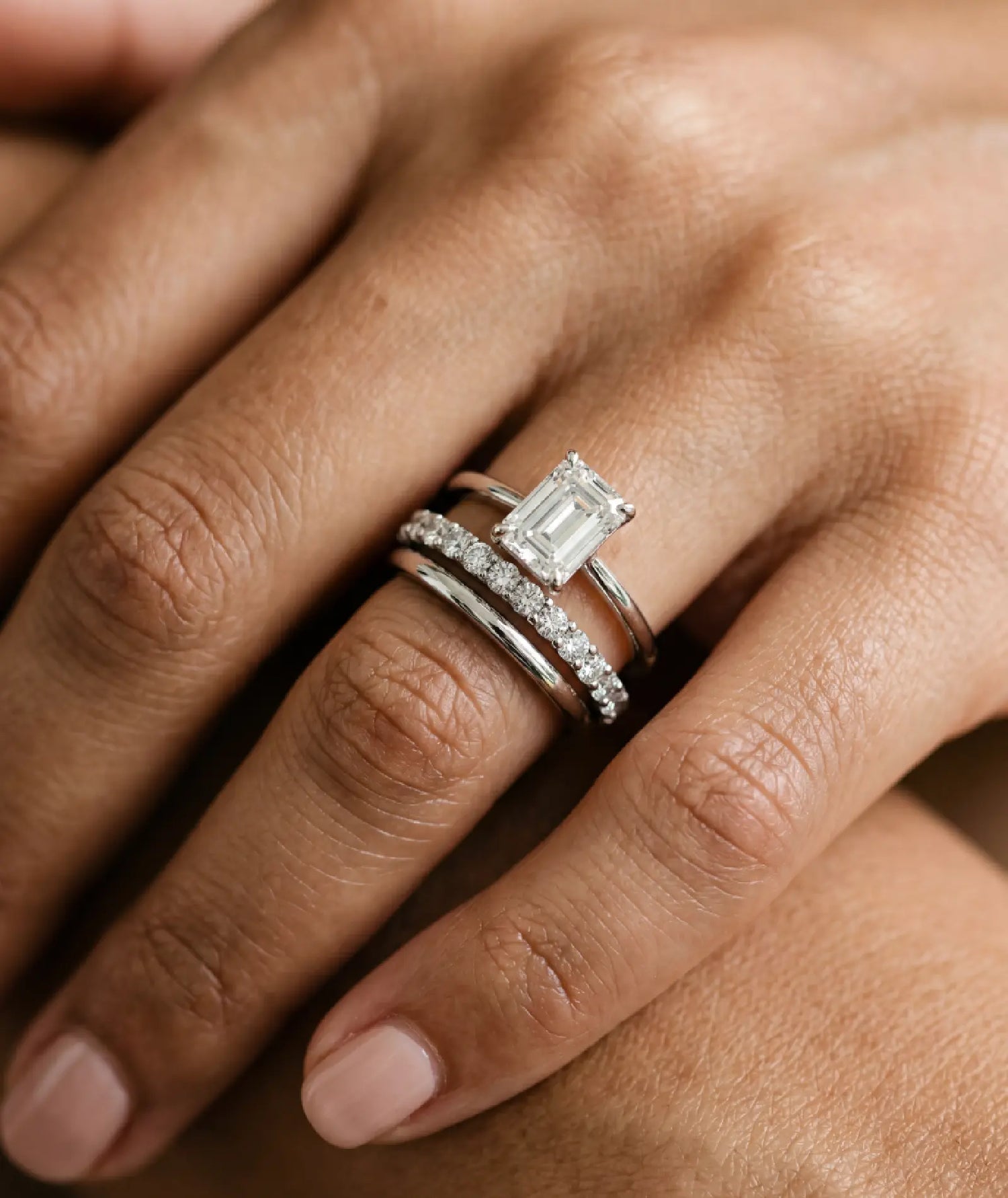 diamantring i hvitt gull med 1 carat emerald cut diamant - sammen med en evighetsring og giftering i hvitt gull, på finger.