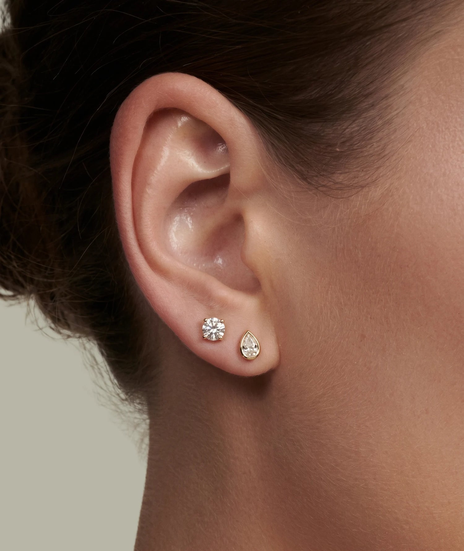 Dråpeformet 0,50 carat diamantøredobb i gult gull bezel og en 0,50 carat rundt diamantøredobb i gult gull på modell.