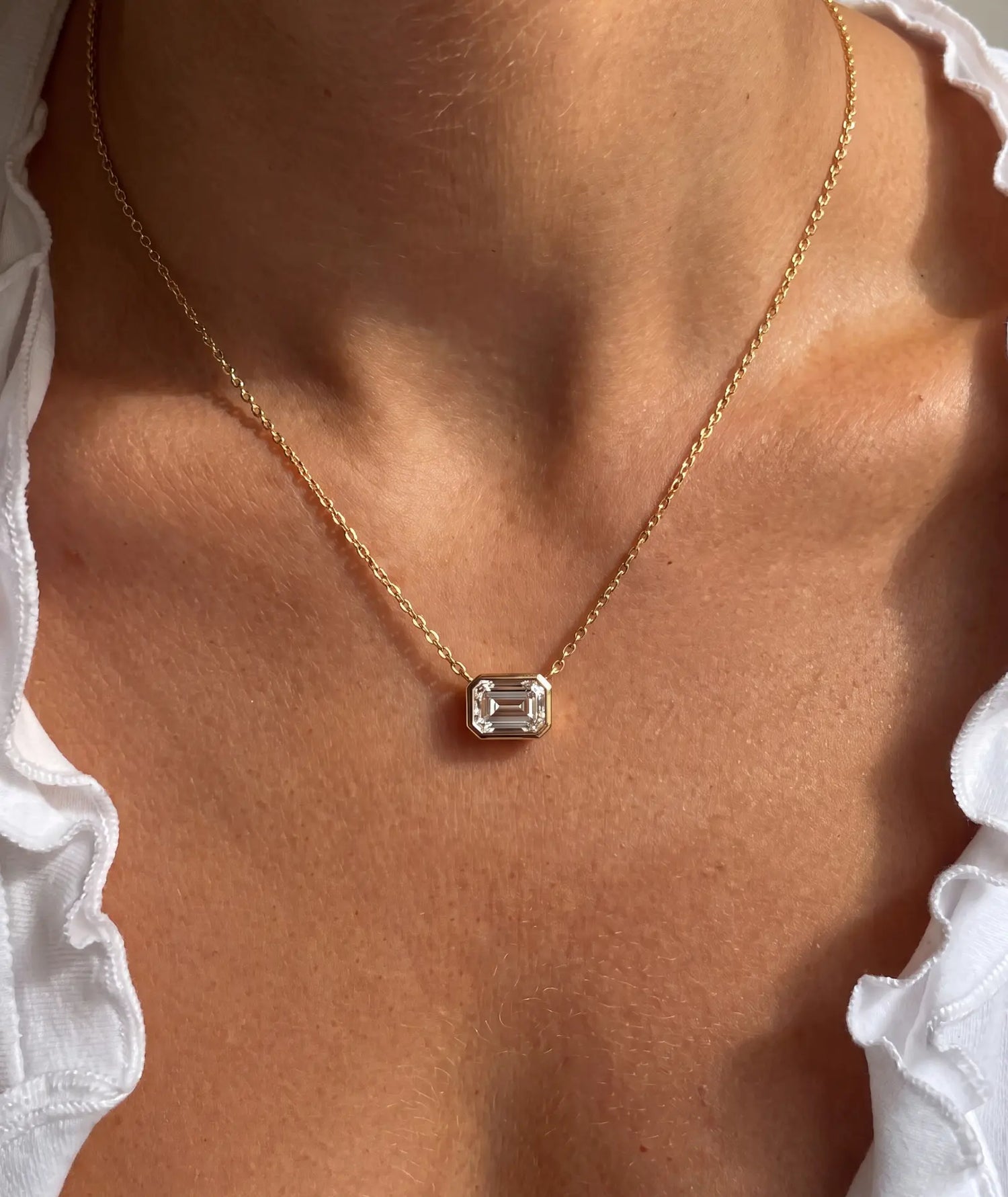 Emerald cut diamanthalskjede i bezelinnfatning, 14K gult gull på modell.