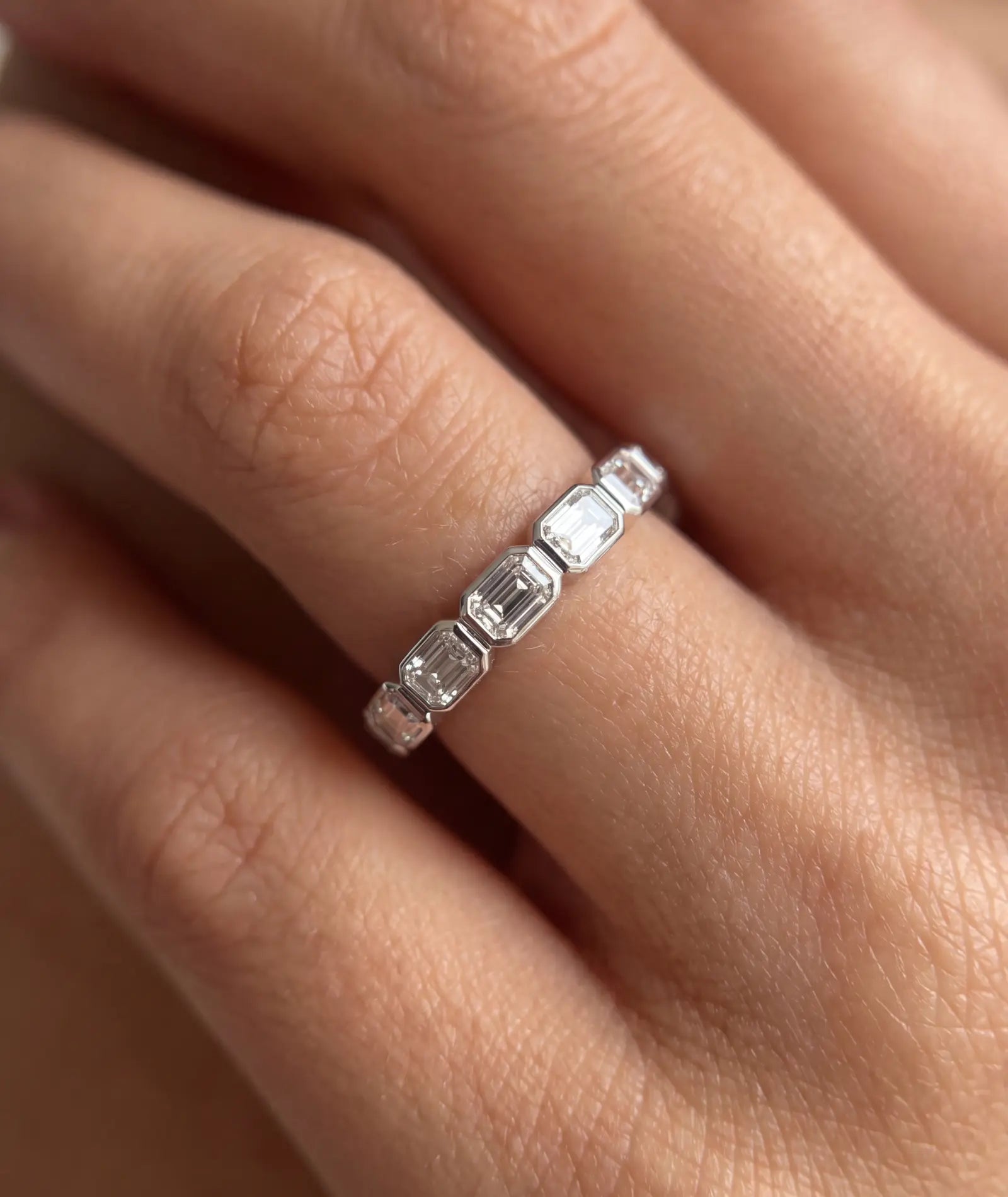 Emerald cut east-west eternity-ring i bezelinnfatning, 14K hvitt gull, nærbilde på finger, 1,40 ct laboratoriedyrkede diamanter.