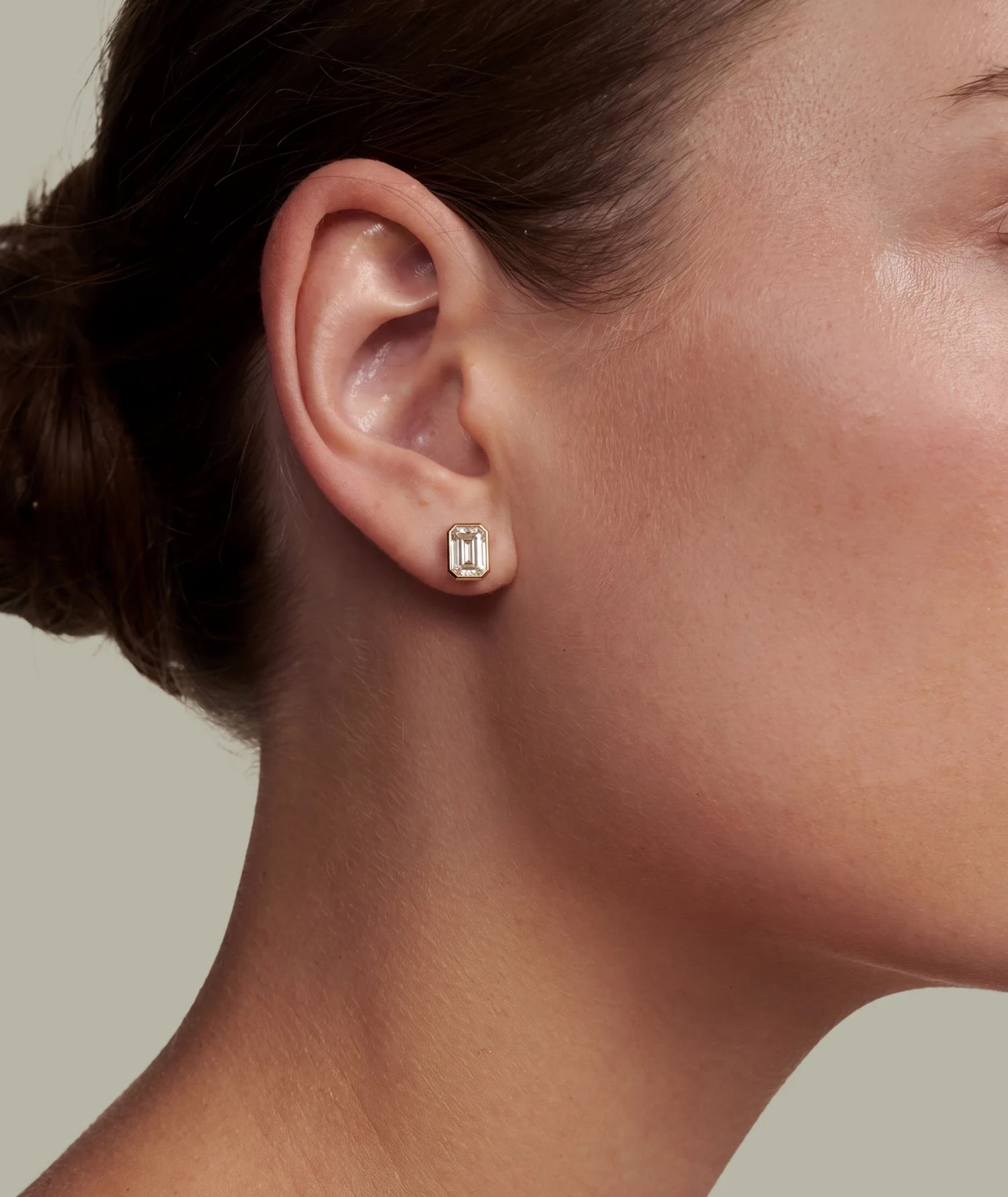 Emerald cut enstens diamantøredobb med bezel gult gull i øret på modell. 