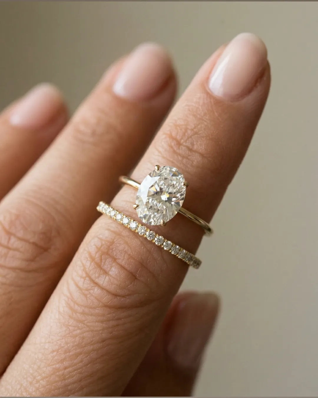 Oval lab-diamant forlovelsesring med slank skinne stablet med pavé giftering i gult gull på ringfingeren.