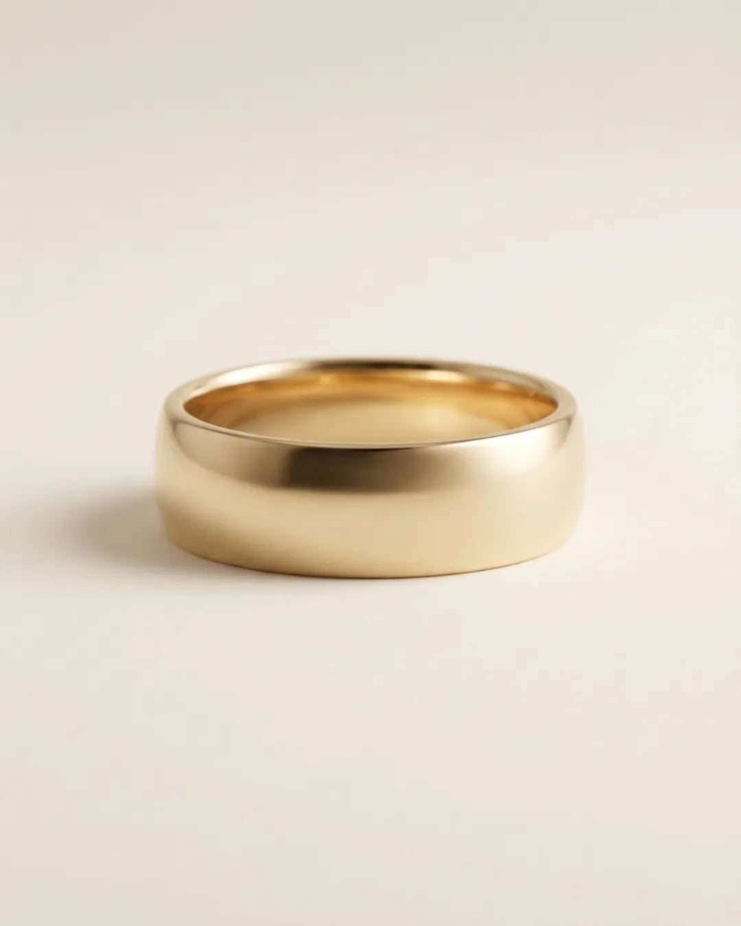 Unisex giftering i polert gult gull, 6 mm bred med buet comfort fit-profil, fotografert mot varm off-white bakgrunn.