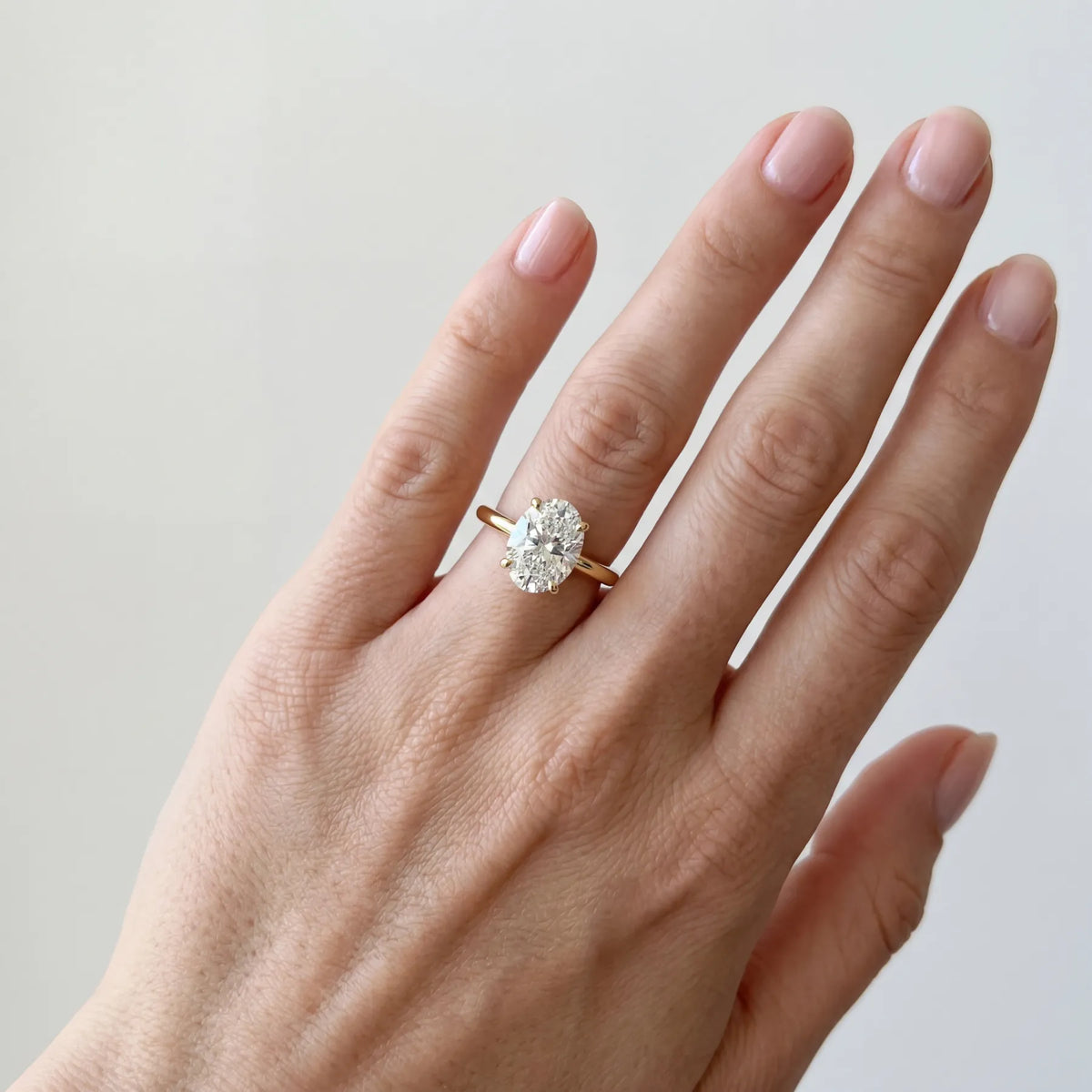 Oval forlovelsesring i gult gull med 2,00 ct lab-diamant. Langstrakt fasong, lav innfatning, på hånden til modell.