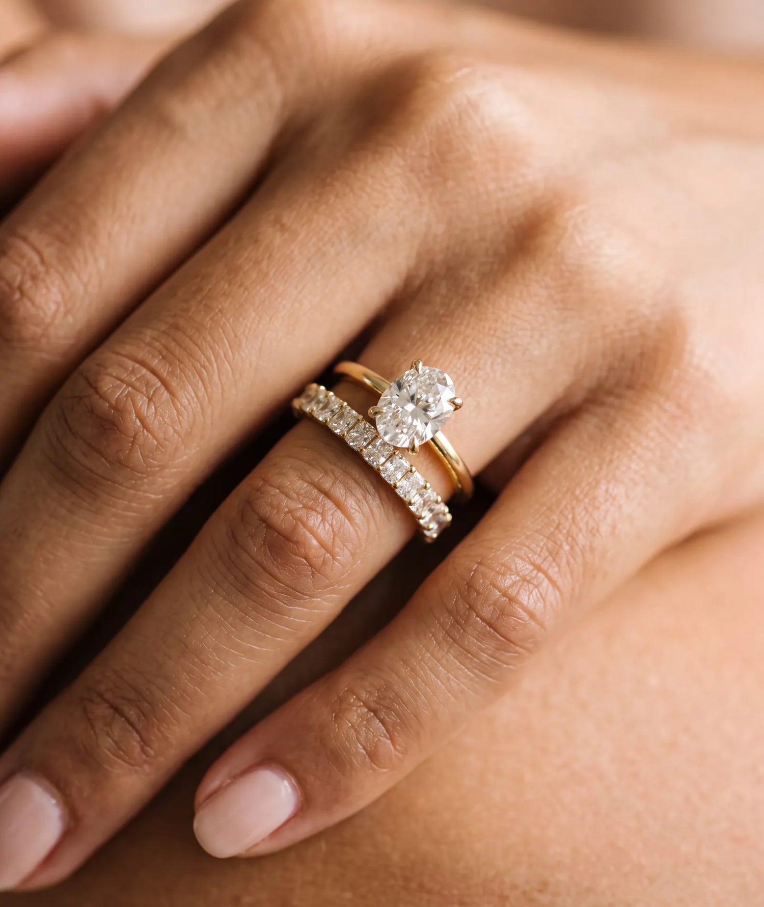 Oval forlovelsesring i gult gull med 2,00 ct lab-diamant. Langstrakt fasong, lav innfatning, på hånden til modell.