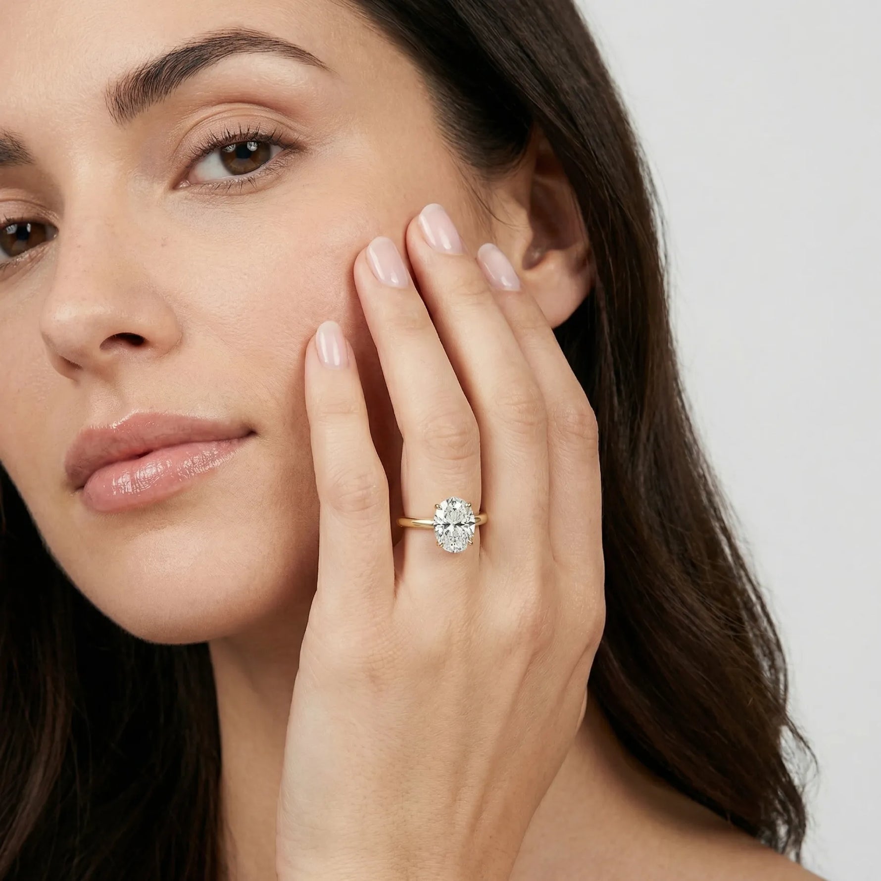 Oval forlovelsesring i gult gull med 2 carat lab diamant vist på modellens hånd i  naturlig lys, med ansikt.
