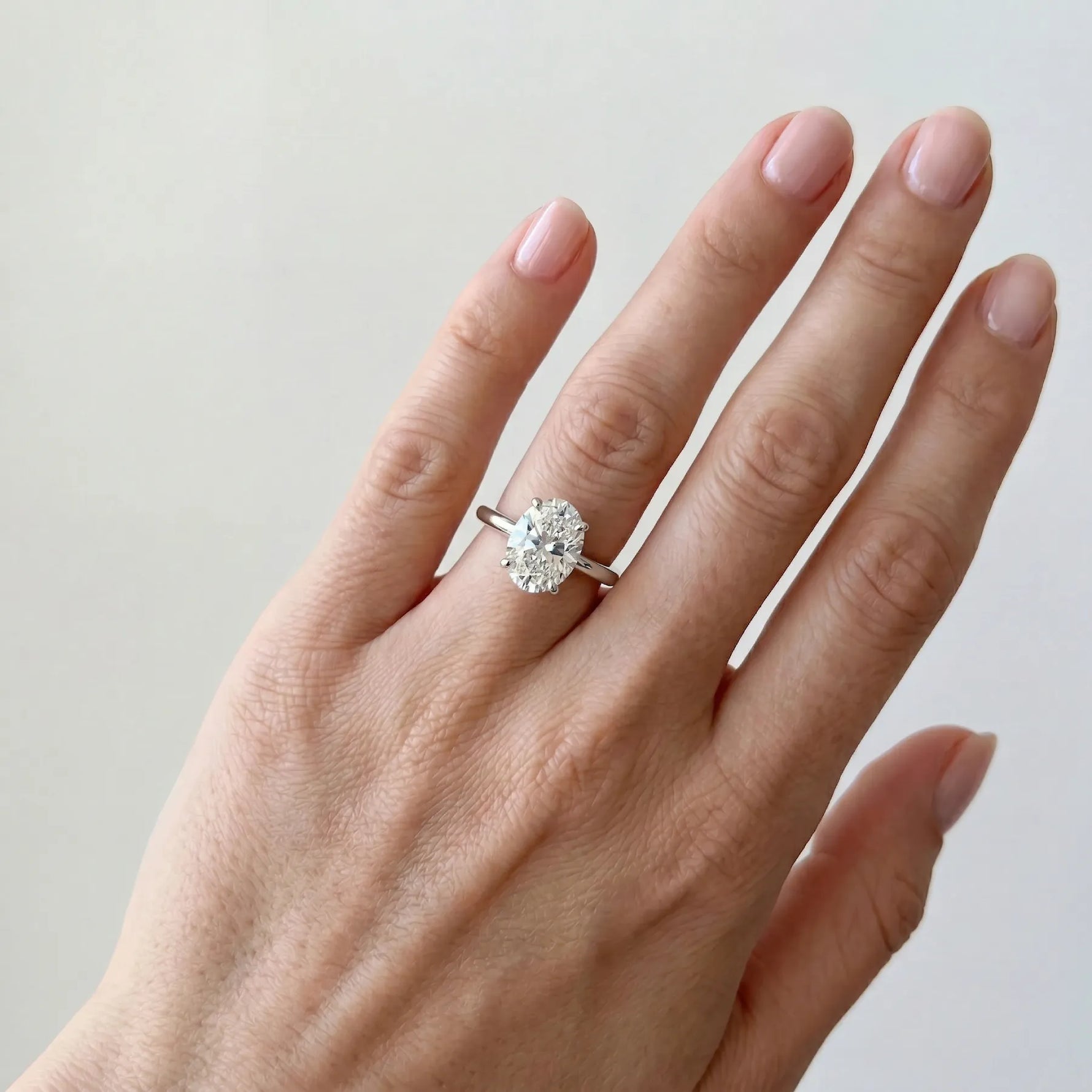 Oval forlovelsesring i hvitt gull 2 carat lab diamantpå hånden til modell i naturlig lys.