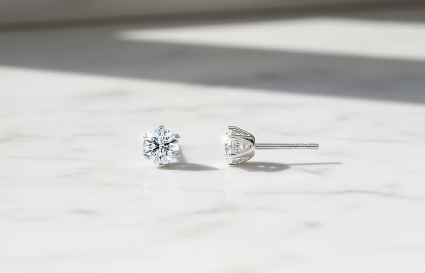 Et par små enstens diamantøredobber i hvitt gull på marmor