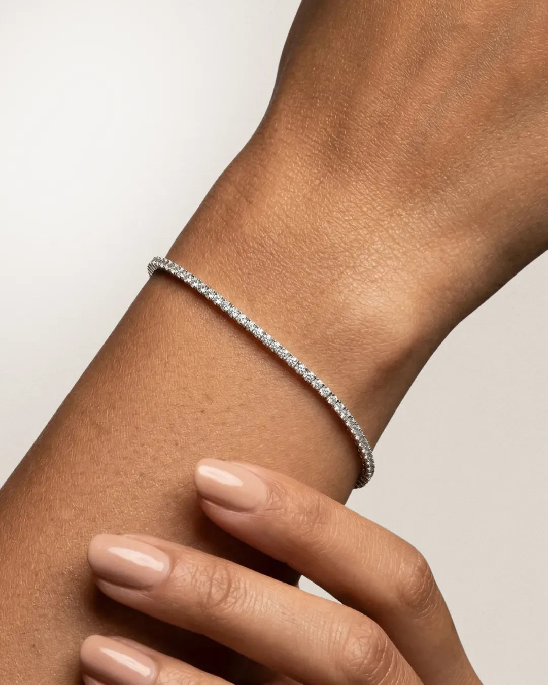 Tennisarmbånd i hvitt gull med 2 carat runde brilliantslipte lab-diamanter i klofatning, båret på håndleddet mot lys nøytral bakgrunn.